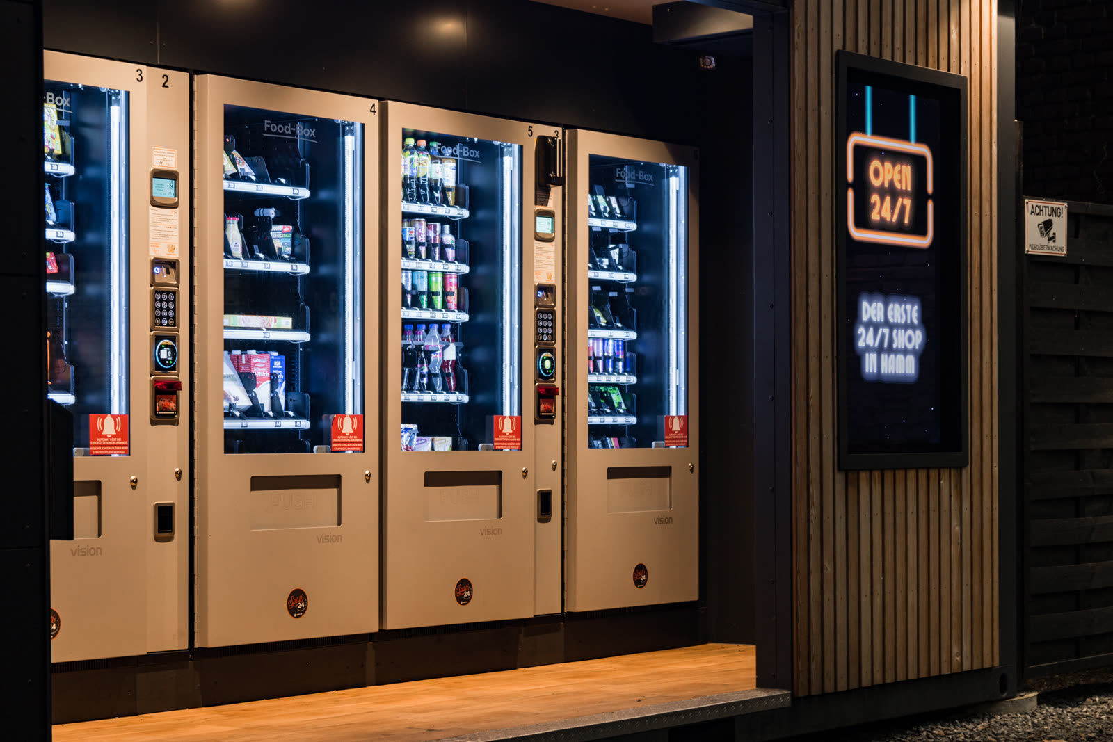 Automatenbank mit Snacks und Getränken, daneben ein Open-24/7-Display