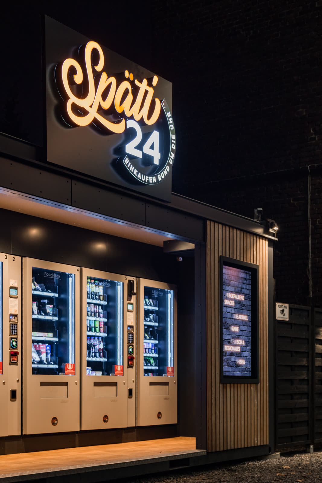 Beleuchteter Späti24-Schriftzug über den Automaten mit Holzfassade